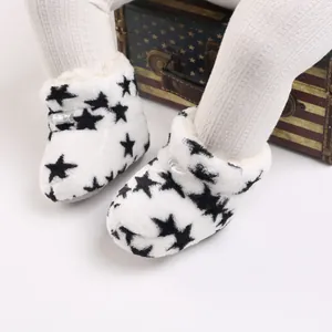 Primer plano de botines de felpa blancos para bebé con estampados de estrellas negras.