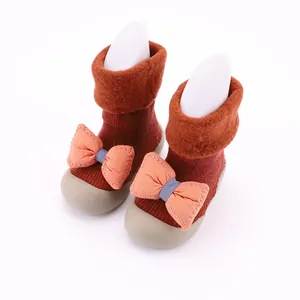 Dettaglio scarpe calzino neonato in maglia con risvolto in peluche e fiocco arancione.