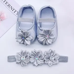 Detailed view of silver satin baby shoes and headband set with ornate fabric flowers