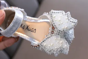Nahaufnahme von silbernen Sandalen für Mädchen mit Schleife aus Perlen und Strass.