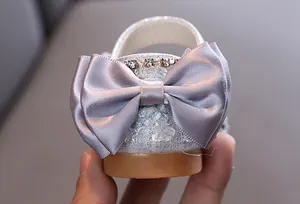 Detailansicht silberner Mädchensandalen mit einer großen Satinschleife und Strass