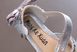 Nahaufnahme von silbernen Mädchenprinzessin-Sandalen mit Strass und Satinschleife Detail