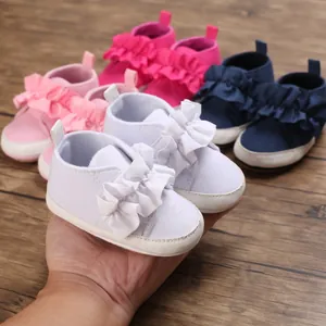 Nahaufnahme eines weißen Babylauflernschuhs mit Rüschendetails in einer Hand gehalten