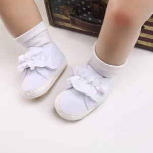 Detailansicht weißer Baby-Lauflernschuhe mit Rüschen und weicher Sohle an Puppenbeinen.