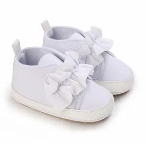 Detailansicht weißer Lauflernschuhe für Babys mit großen dekorativen Rüschenschleifen.