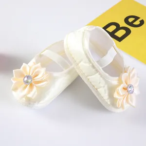 Nahaufnahme von cremefarbenen Baby-Prinzessin-Schuhen aus Satin mit Blumen- und Strassdetail
