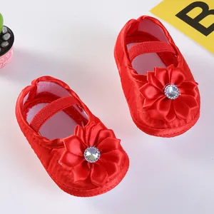 Nahaufnahme roter Baby-Prinzessinenschuhe aus Satin mit großer Blume und Strass.