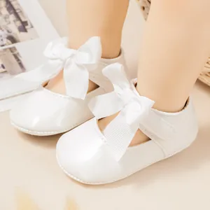 Primer plano de zapatos de charol blanco para bebé con grandes lazos decorativos.