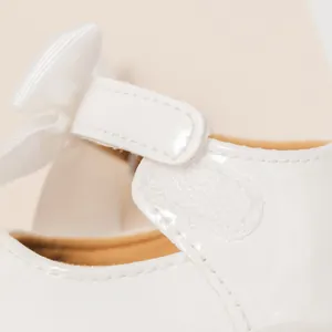 Primer plano de zapato de charol blanco para bebé con cierre de velcro y lazo