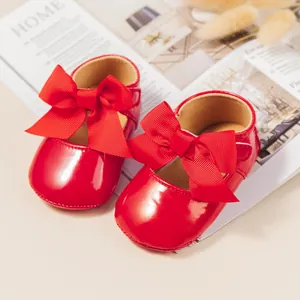 Detalle de zapatos de bebé rojos brillantes con lazo grande sobre un fondo estético.