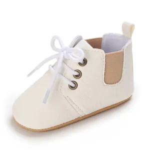 Vista lateral de un zapato de bebé blanco con suela blanda y diseño de cordones