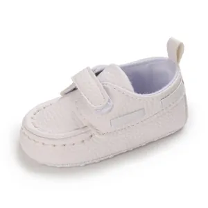 Nahaufnahme von weißen Babyschuhen mit weicher Sohle und Klettverschluss.