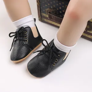 Primer plano de pies de bebé con zapatos de cuero negro con suela blanda y cordones.