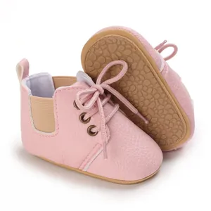 Primer plano de zapatos de bebé rosa en cuero sintético con suela de goma blanda y cordones