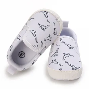 Detailopname van witte baby loopschoentjes met dinosaurusprint en zachte getextureerde zolen.