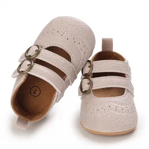 Close-up of beige faux leather baby shoes with decorative brogue details and buckles.
