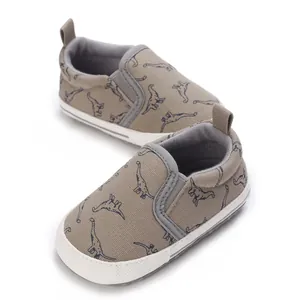 Soft-soled baby walking shoes with navy dinosaur pattern on khaki canvas upper.