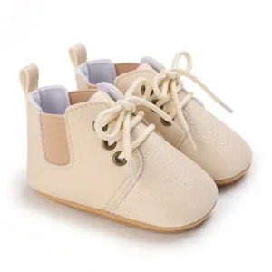 Primer plano de zapatos para bebé crema con suela blanda y diseño de cuero sintético.