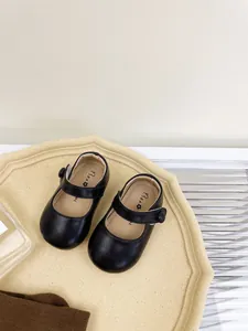 Close-up detail of black leather soft-sole baby walking shoes on an elegant beige tray