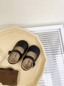 Top-down detail of black soft-sole Mary Jane shoes for baby girls on a beige tray.