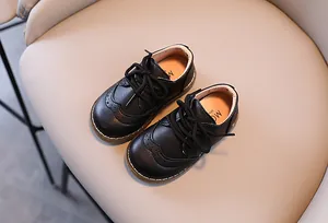 Draufsicht auf schwarze Brogue-Kinderschuhe mit Schnürung auf beigem Untergrund