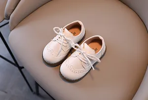 Draufsicht auf weiße Kinderlederschuhe im britischen Stil auf einem beigen Lederstuhl.