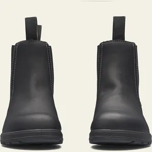 Vista frontal de botas Chelsea de cuero negro mate con tiradores sobre fondo crema