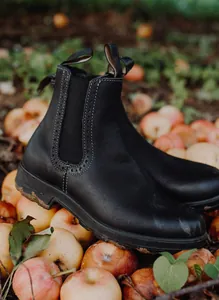 Primer plano de botas Chelsea de cuero negro con detalles brogue en un entorno natural