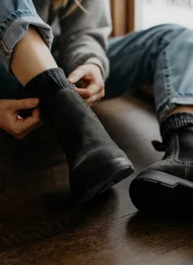 Primer plano de una mujer usando botas Chelsea de cuero mate oscuro en suelo de madera