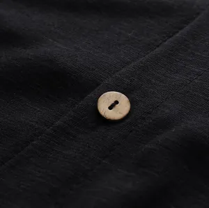Close-up macro detail of a black textured fabric jumpsuit with a natural wooden button.