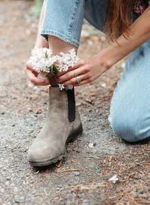 Primer plano de botas Chelsea de cuero marrón vintage con flores en entorno natural