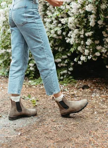 Detalle de botines Chelsea de cuero marrón para mujer usados con vaqueros al aire libre.