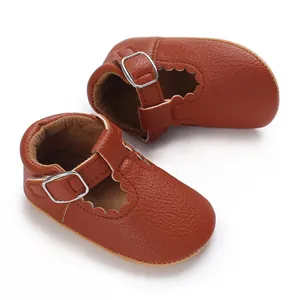 Close-up of brown leather baby t-strap shoes showing texture and metal buckles.