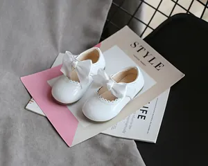 Nahaufnahme von weißen Lacklederschuhen für Mädchen mit großen Satinschleifen.