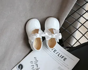 Draufsicht auf weiße Lacklederschuhe für Mädchen mit großen Schleifen auf einem Magazin.