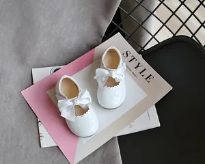 Nahaufnahme von weißen Lacklederschuhen für Kleinkinder mit großen Schleifen.