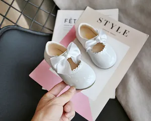 Nahaufnahme von weißen Lacklederschuhen für Babys mit Satin-Schleifen