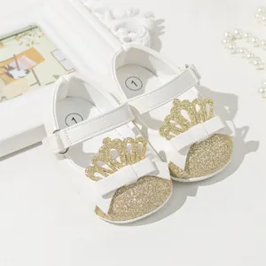 Close-up of white baby walker shoes featuring gold glitter toe caps and crown decorations