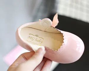 Nahaufnahme eines Mädchenschuhs aus rosa Lackleder mit Wellenkanten und goldenem Logo