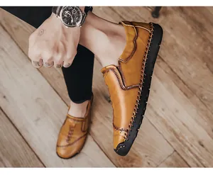 Handgestikte bruine casual herenloafers op model met houten vloer achtergrond