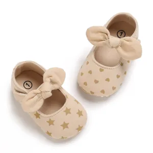 Close-up of baby beige cotton shoes with gold star and heart patterns and bows