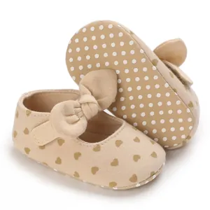 Detailed view of baby girl walker shoes featuring heart prints, a large bow, and soft dot soles