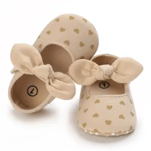 Close-up detail of beige baby cotton shoes with heart patterns and decorative fabric bows