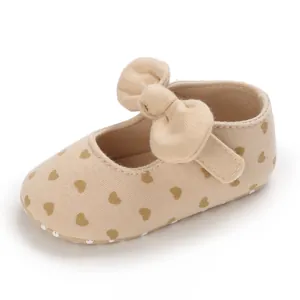 Detail view of beige baby girl walking shoe with brown heart print and decorative bow.