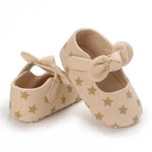 Close-up of beige baby walking shoes with gold star prints and cute bow details