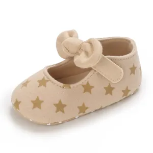 Macro detail of beige baby girl Mary Jane shoe with gold star print and soft cotton bow