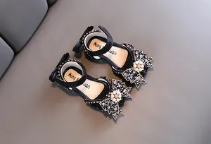 Detail view of black girls' princess sandals with rhinestone bow and pearl accents