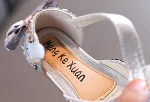 Close-up macro detail of silver girls' princess sandal featuring rhinestones and a bow