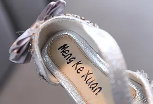 Close-up detail of the elegant silver rhinestone bow and brand logo on girls' princess sandals