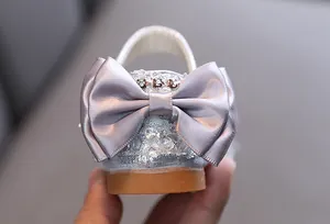 Detailed close-up of silver girl princess shoes featuring a satin bow and rhinestones